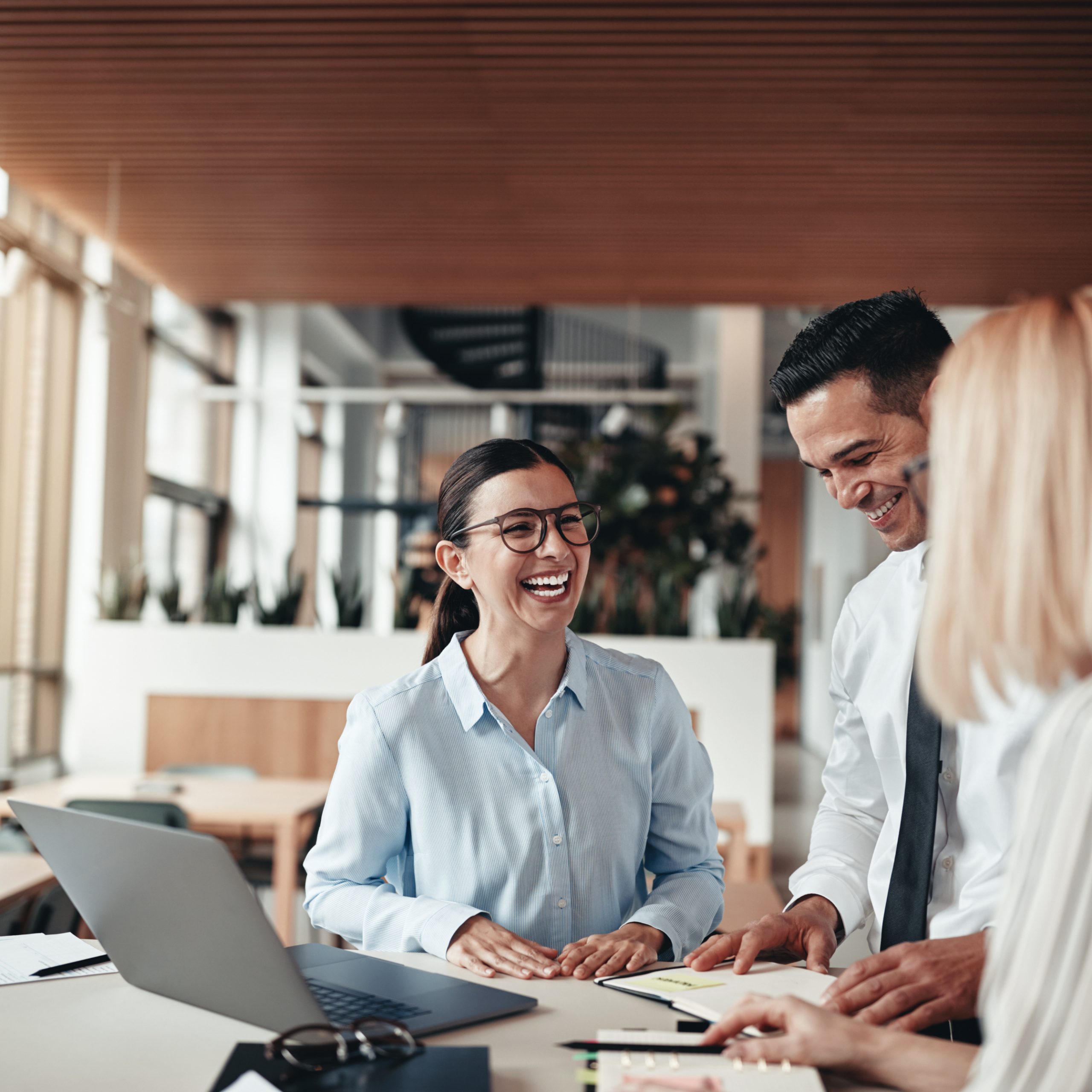 I & J Refrigeration Ltd | Businesspeople laughing while working at an office table Interior room with ceiling-mounted cassette type air conditioner and modern ceiling lamp, suitable for home and business cooling in the Okanagan